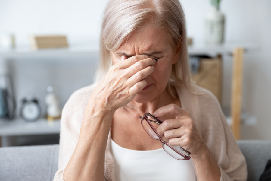 Woman holding her eyes with her glasses in the other hand depicting chronic pain.