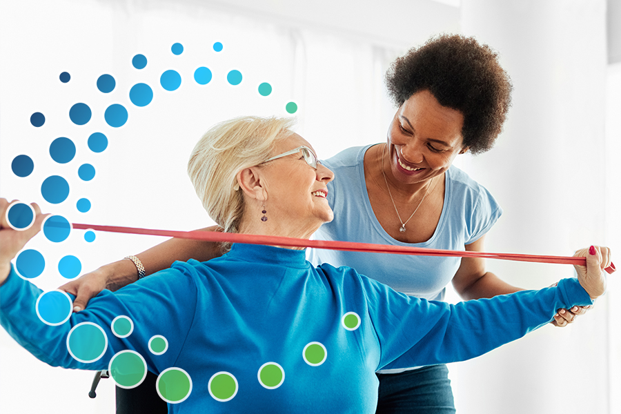 Woman assisting another woman with physical therapy using stretch bands in a medical setting.