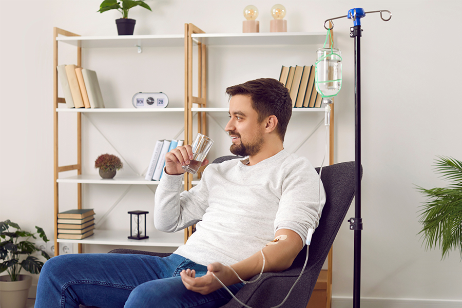 Man sitting in a comfortable chair receiving an IV therapy treatment while drinking a glass of water.